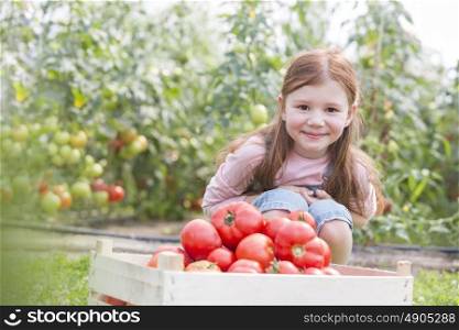 Portrait of smiling girl with fresh organic tomatoes in crate at farm