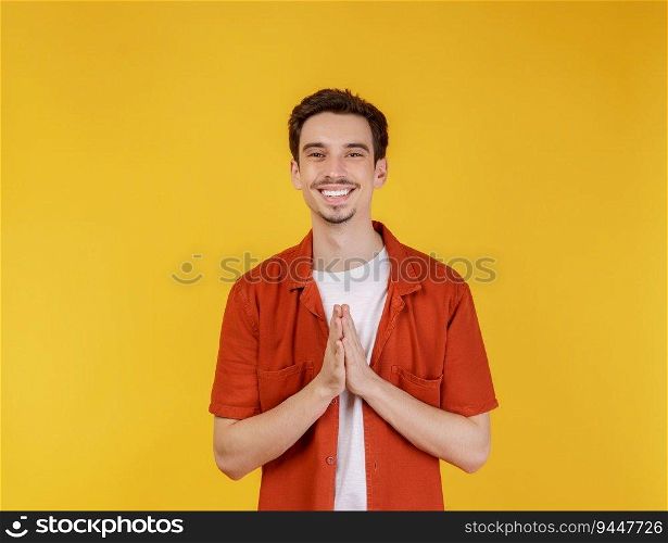 Portrait of smiling handsome man in pay respect pose, standing over yellow background. People and lifestyle concept.