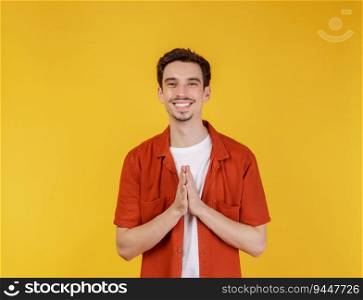 Portrait of smiling handsome man in pay respect pose, standing over yellow background. People and lifestyle concept.