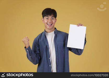 portrait of smiling happy cheerful young asian man dressed casually showing blank empty placard paper isolated on yellow studio background.