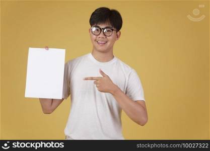 portrait of smiling happy cheerful young asian man dressed casually showing blank empty placard paper isolated on yellow studio background.