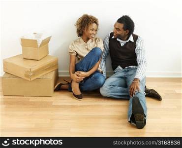 Portrait of smiling happy young couple sitting on floor of home with moving boxes.