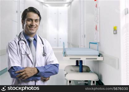 Portrait of smiling male doctor standing arms crossed in hospital corridor