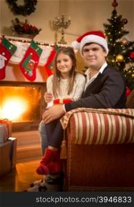 Portrait of smiling man and girl relaxing on sofa at fireplace at Christmas eve