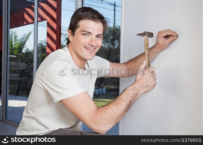 Portrait of smiling man hammering the wall with nail