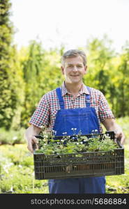 Portrait of smiling man holding crate of potted plants at garden