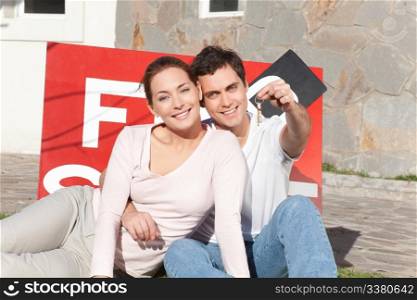 Portrait of smiling man holding keys with wife sitting on side