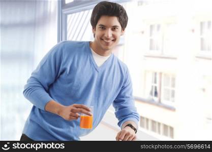 Portrait of smiling man leaning on window while holding glass of orange juice