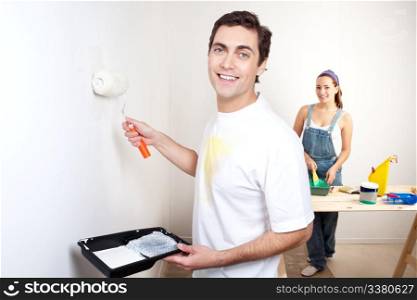 Portrait of smiling man painting the wall with woman standing in the background