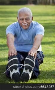 Portrait of smiling man stretching in park
