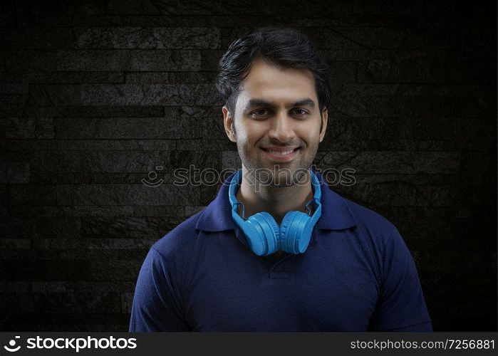 Portrait of smiling man with headphones on neck over black background