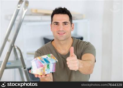 portrait of smiling man with house model gesturing thumbs up