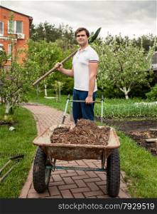 Portrait of smiling man with spade and garden wheelbarrow