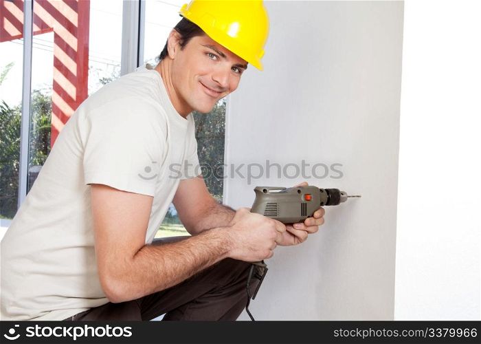 Portrait of smiling man worker with hard hat drilling wall