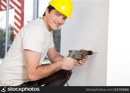 Portrait of smiling man worker with hard hat drilling wall