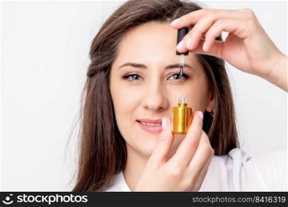 Portrait of smiling manicure master holds gold nail varnish bottle over her eye on white background. manicurist holds nail varnish bottle