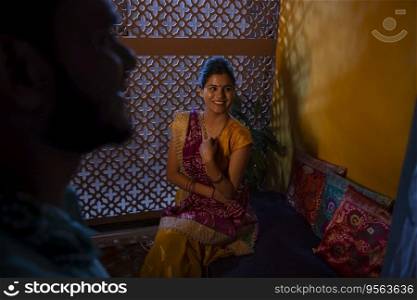 Portrait of smiling married Gujrati woman sitting on deewan and looking at her husband