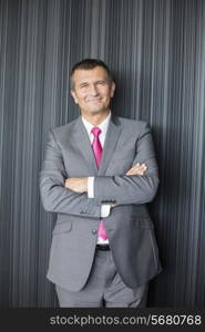 Portrait of smiling mature businessman standing arms crossed against wall
