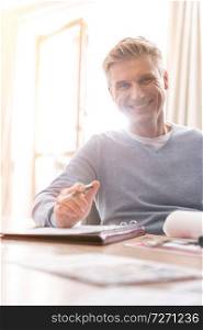 Portrait of smiling mature man sitting with document at table in apartment