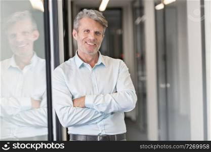 Portrait of smiling mature man standing with arms crossed at office