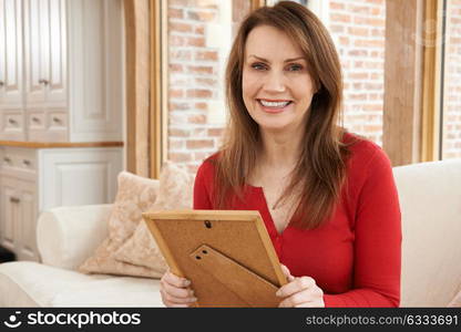 Portrait Of Smiling Mature Woman Looking At Picture Frame At Home