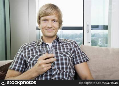 Portrait of smiling mid-adult man with glass of drink on sofa at home