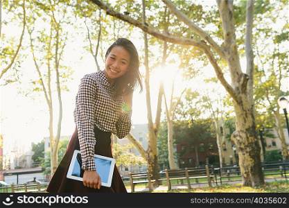Portrait of smiling mid adult woman carrying digital tablet in city park
