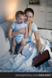 Portrait of smiling mother and adorable baby reading book before going to sleep
