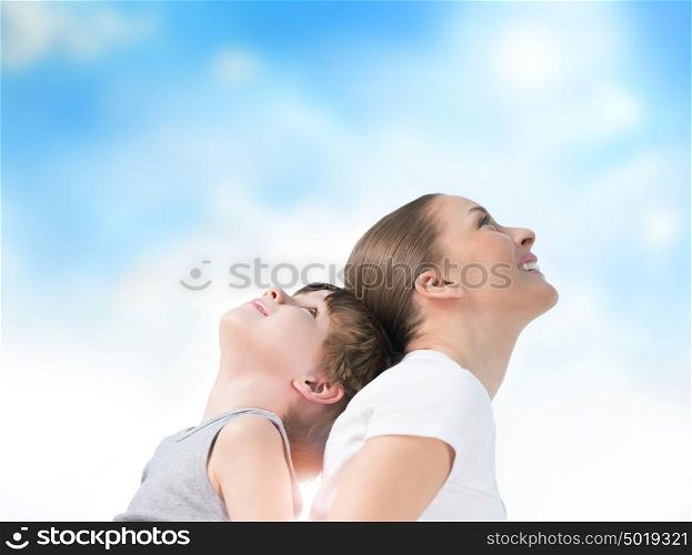 Portrait of smiling mother and her son standing back to back outdoors against sky
