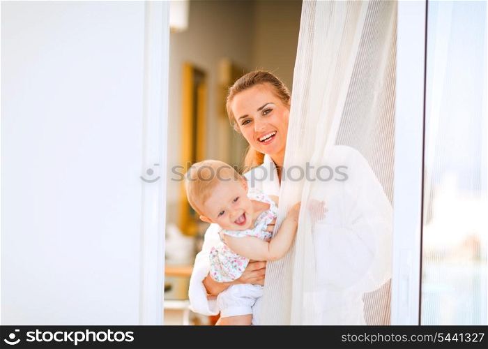 Portrait of smiling mother in bathrobe with baby looking out from window&#xA;