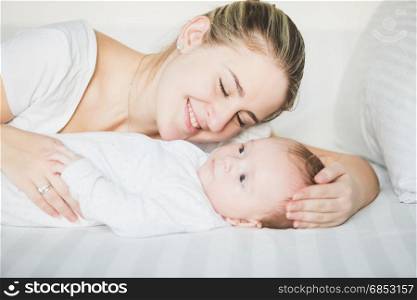Portrait of smiling mother lying with 3 months old baby on bed