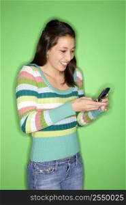 Portrait of smiling Multi-racial teen girl dialing cellphone standing in front of green background.