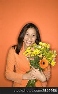 Portrait of smiling Multi-racial teen girl with bouquet of flowers standing against orange background.