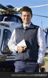 Portrait Of Smiling Pilot Standing In Front Of Helicopter With Digital Tablet