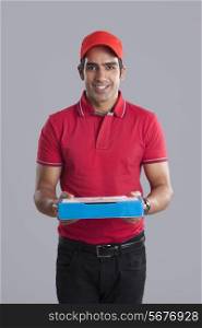 Portrait of smiling pizza delivery man against gray background