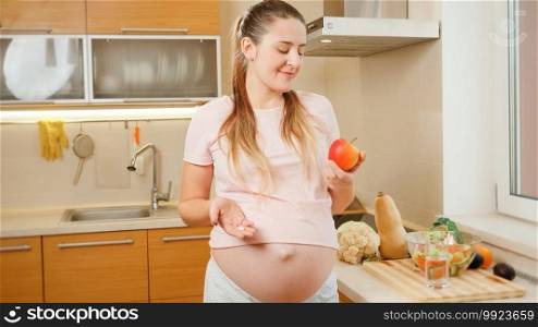 Portrait of smiling pregnant woman choosing between eating fresh apple or taking vitamin pills. Concept of healthy lifestyle, nutrition and hydration during pregnancy.. Portrait of smiling pregnant woman choosing between eating fresh apple or taking vitamin pills. Concept of healthy lifestyle, nutrition and hydration during pregnancy