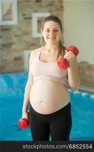 Portrait of smiling pregnant woman lifting up dumbbells
