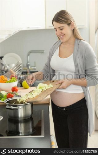 Portrait of smiling pregnant woman putting vegetables in soup