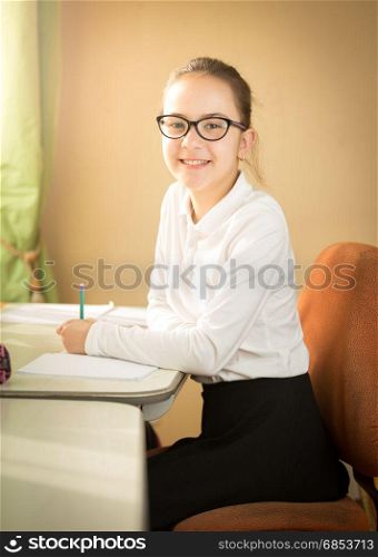 Portrait of smiling schoolgirl posing behind table at classroom