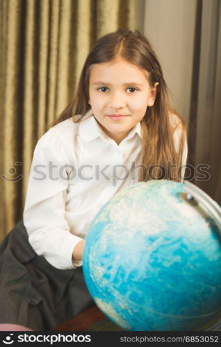 Portrait of smiling schoolgirl posing with Earth globe at cabinet