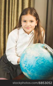 Portrait of smiling schoolgirl posing with Earth globe at cabinet