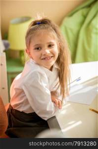 Portrait of smiling schoolgirl sitting at desk in bedroom