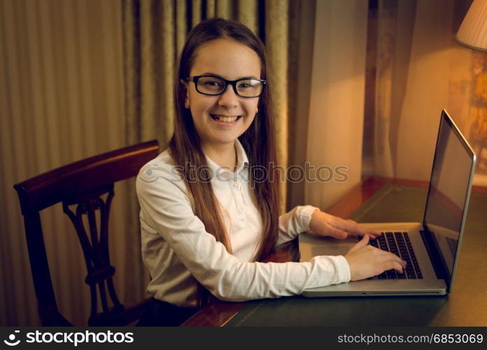 Portrait of smiling schoolgirl using laptop at dark room