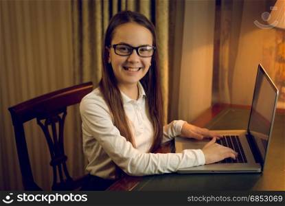 Portrait of smiling schoolgirl using laptop at dark room