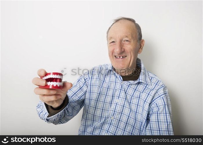 Portrait of smiling senior man holding teeth model against gray background