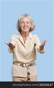 Portrait of smiling senior woman in casuals gesturing against blue background