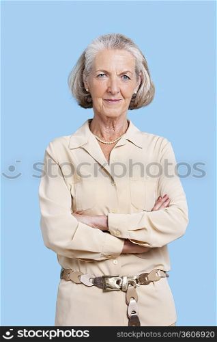 Portrait of smiling senior woman in casuals with arms crossed against blue background