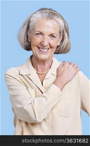 Portrait of smiling senior woman in casuals with hand on shoulder against blue background