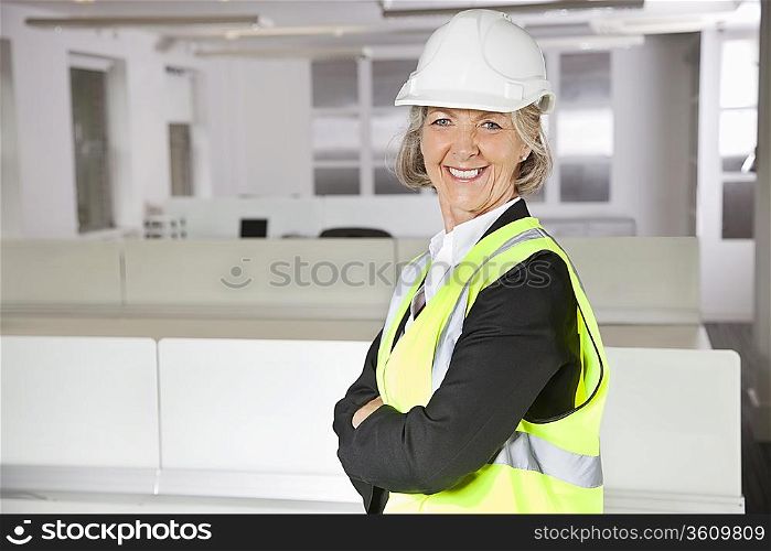 Portrait of smiling senior woman in reflector vest and hard hat at office