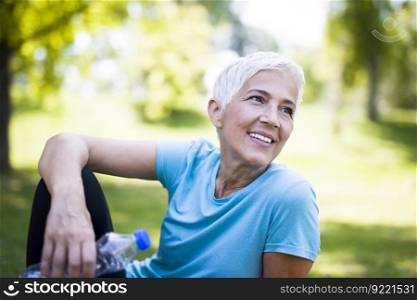 Portrait of smiling senior woman relaxing after exercising while sitting on grass